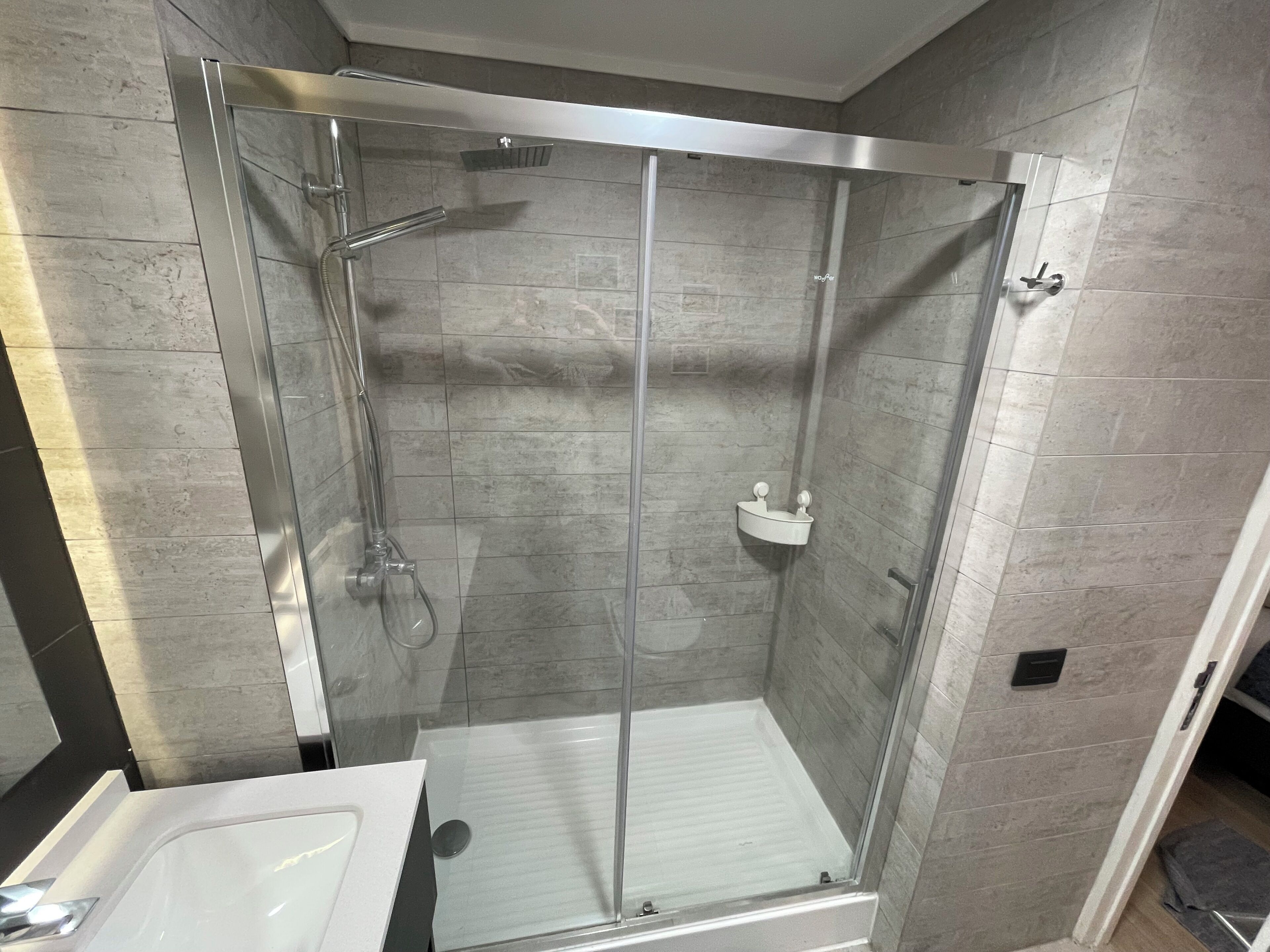 Une salle de bain moderne avec une douche à parois de verre, un lavabo blanc et un sol carrelé.