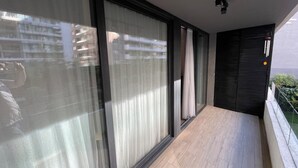 Un balcón con amplias puertas correderas de vidrio, una lámpara moderna y vista a un edificio de la calle.