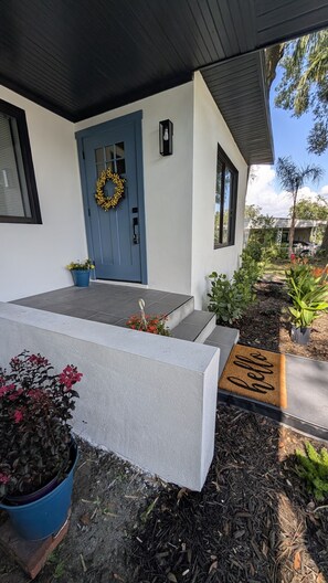 A modern house with a blue door, a welcome mat, and potted plants. - Casa Linda Cottage (Temple Terrace)