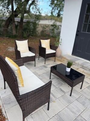 Eine Terrasse mit Korbmöbeln, einem Glastisch und einem Blumentopf.