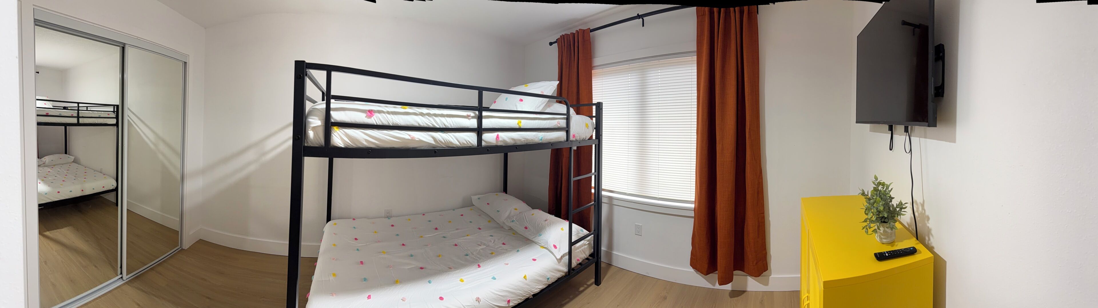 A bunk bed room with a mirror, a TV, and a yellow side table with a plant.