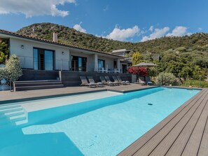 Eine moderne Villa mit Swimmingpool, einer Terrasse und einer Hügelkulisse.