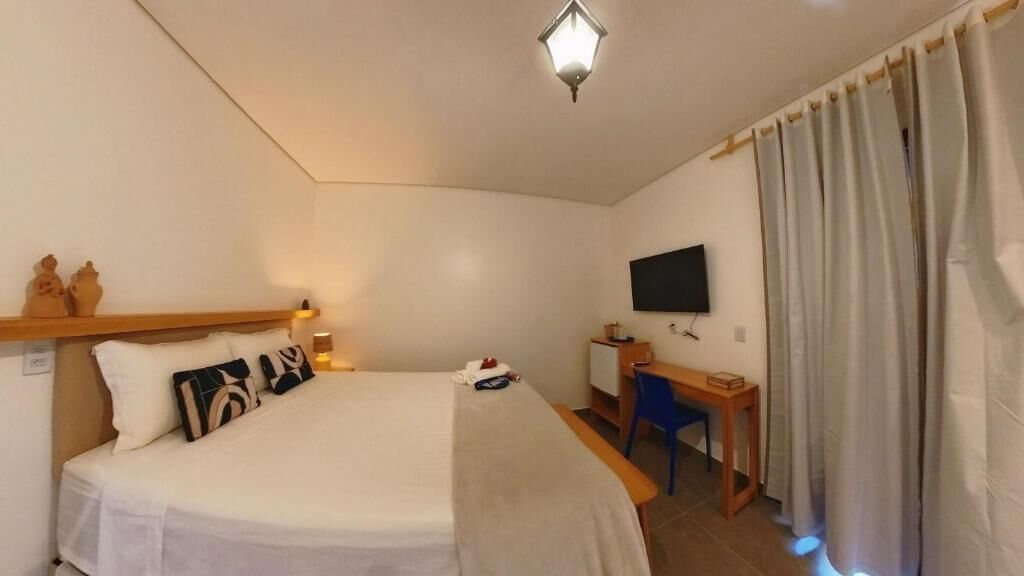 A hotel room with a bed, a desk, a television, and curtains.
