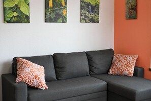 Ein dunkelgraues Modulsofa mit gemusterten Kissen, eine weiße Wand und drei gerahmte Pflanzenbilder.