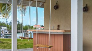 A covered outdoor area with a swing set, a wooden bench, and a view of a body of water. - Bahamas Escape - Pool, Canal, Dockage, Beach (Freeport, Grand Bahama)