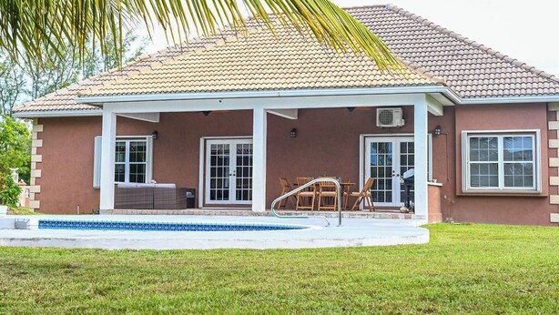 A house with a covered patio, a swimming pool, and a door leading to a covered outdoor area. - Bahamas Escape - Pool, Canal, Dockage, Beach (Freeport, Grand Bahama)