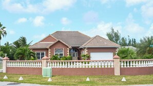 A two-story house with a tiled roof, a garage, and a white fence. - Bahamas Escape - Pool, Canal, Dockage, Beach (Freeport, Grand Bahama)