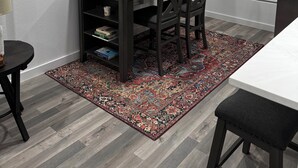 Um quarto com mesa de jantar, cadeiras, estante e tapete estampado.