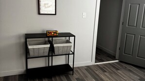 Quarto com piso de madeira, prateleira de metal preta com cestos, um quadro na parede e uma porta.