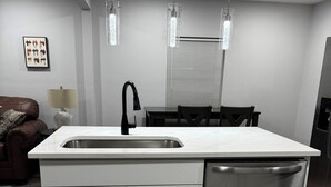 Uma cozinha moderna com pia de aço inoxidável, armários brancos e máquina de lavar louça embutida.