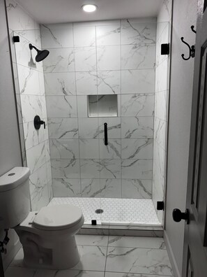 Ein Badezimmer mit Toilette, einer Dusche mit Glastür und einem kleinen Spiegel an der Wand.