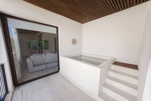 Ein modernes Interieur mit einer Glastür, die in einen Wohnbereich führt, einer weißen Wand mit einem kleinen Regal und einer Holzbalkendecke.