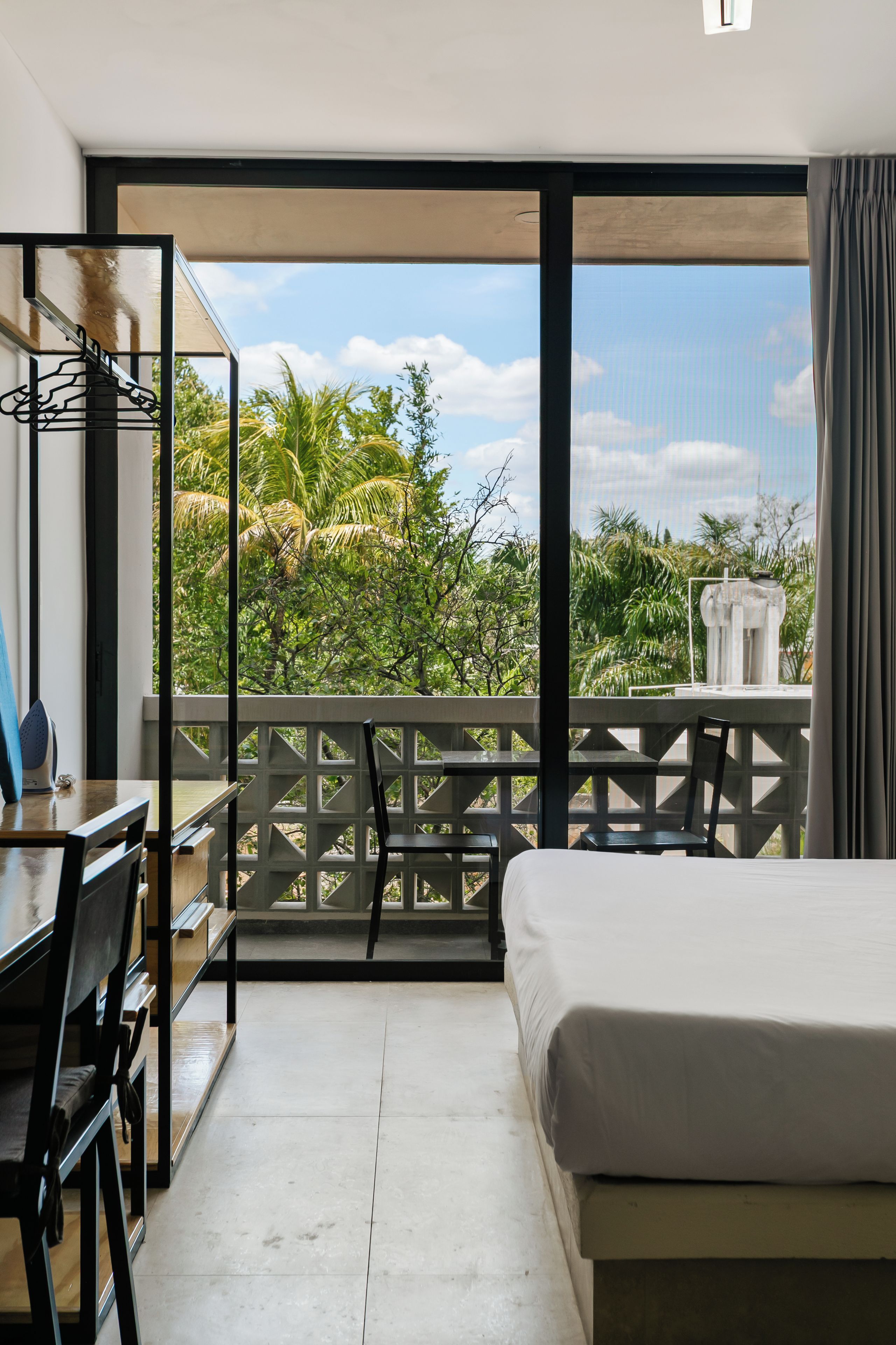 A hotel room with a balcony, a bed, a desk with a chair, and a hanging coat rack.