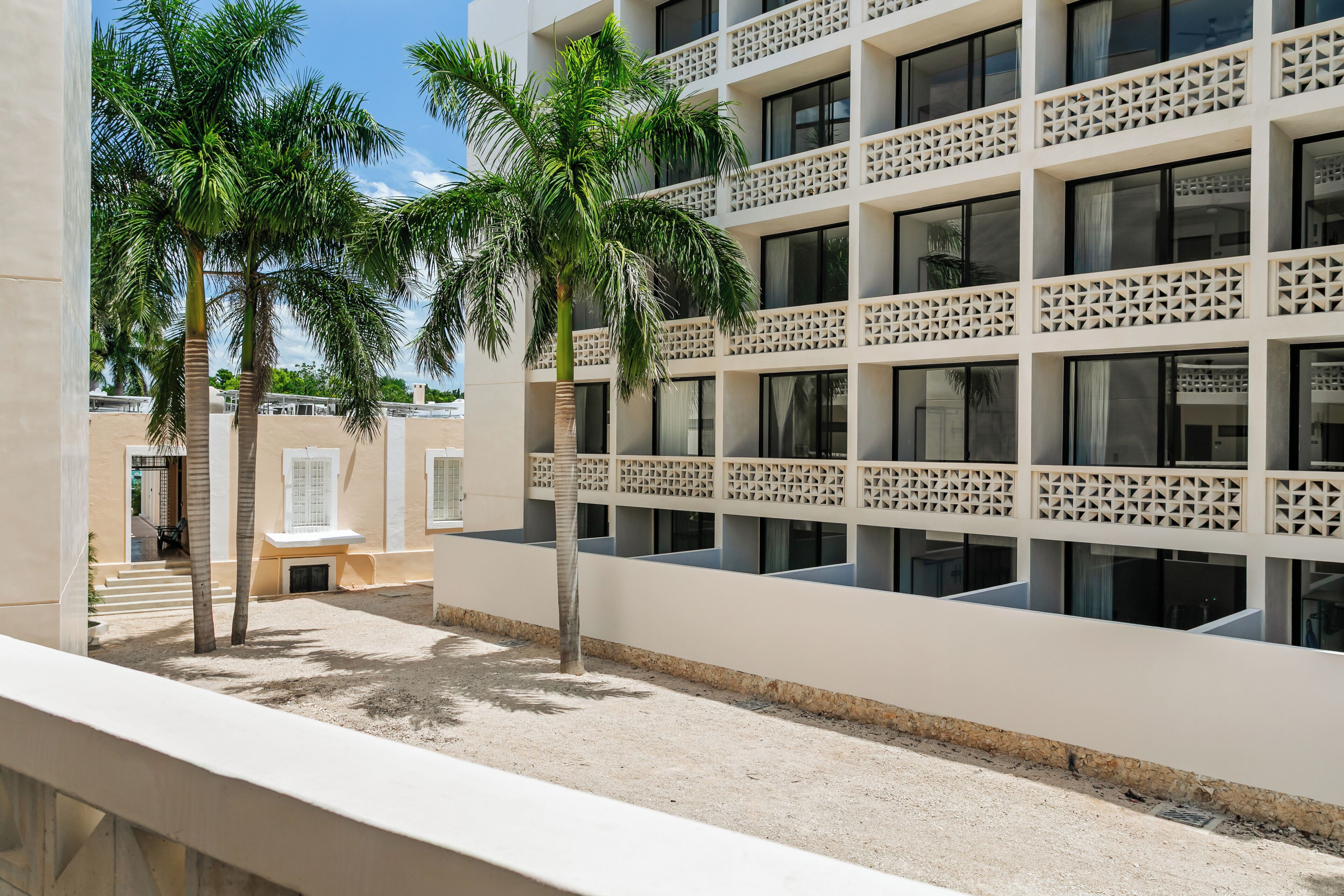 A modern building with multiple balconies, palm trees, and a clear sky.