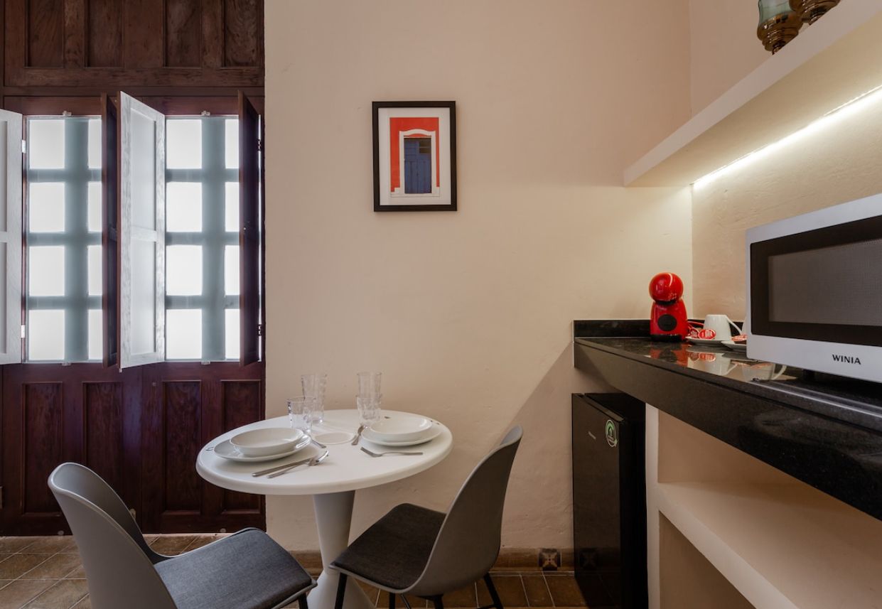 Een eetgedeelte met een ronde tafel, stoelen, een televisie en een ingelijst schilderij aan de muur.