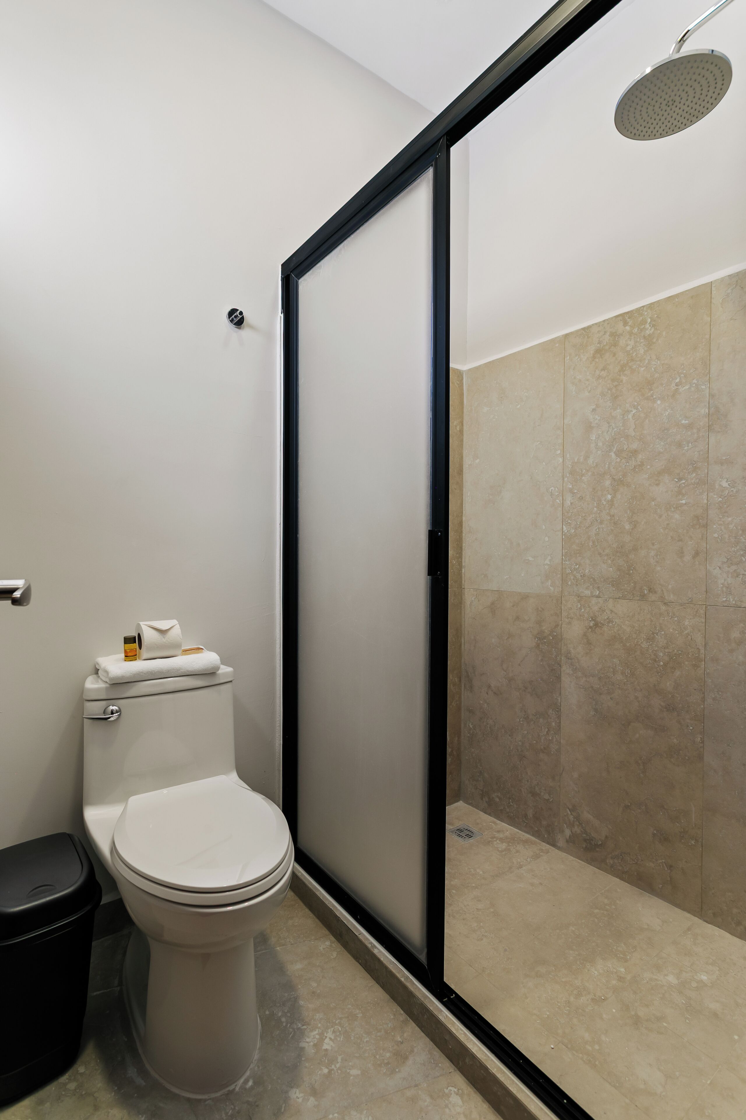 Un baño moderno con inodoro, cabina de ducha y suelo de baldosas.
