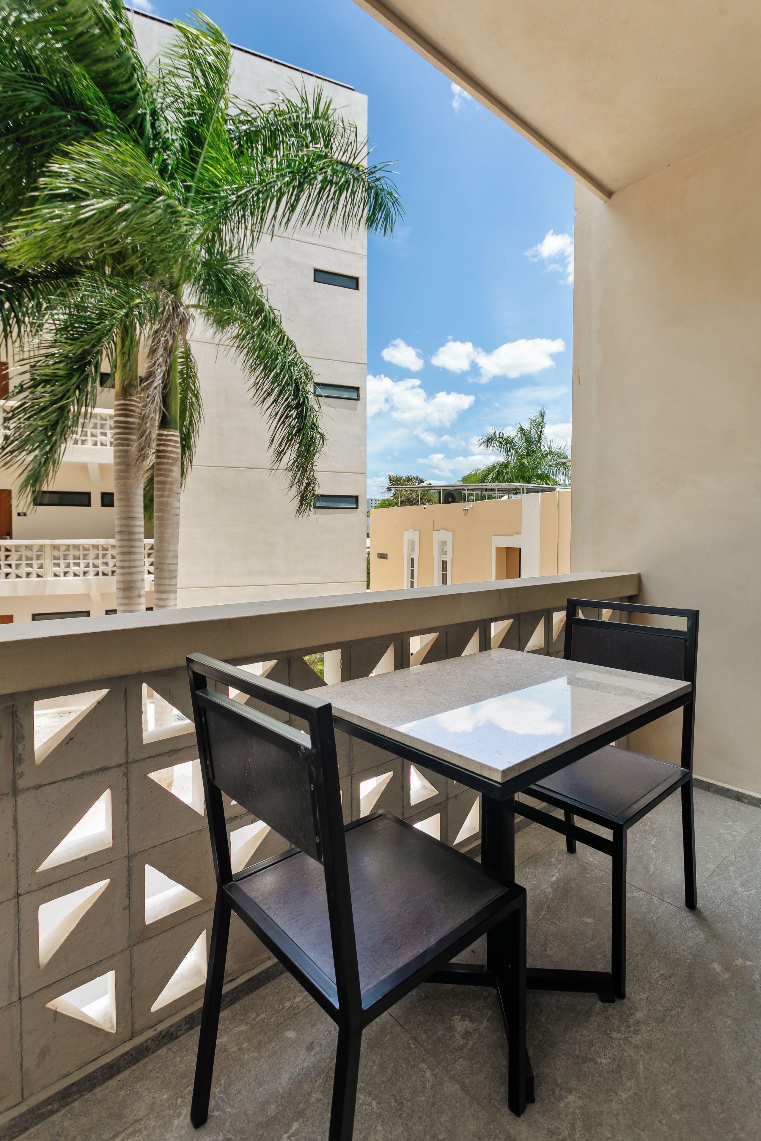A balcony with a table and chairs, a palm tree, and a view of buildings.