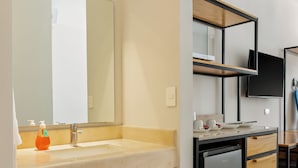 Un baño moderno con lavamanos, espejo, toallero y un refrigerador pequeño.