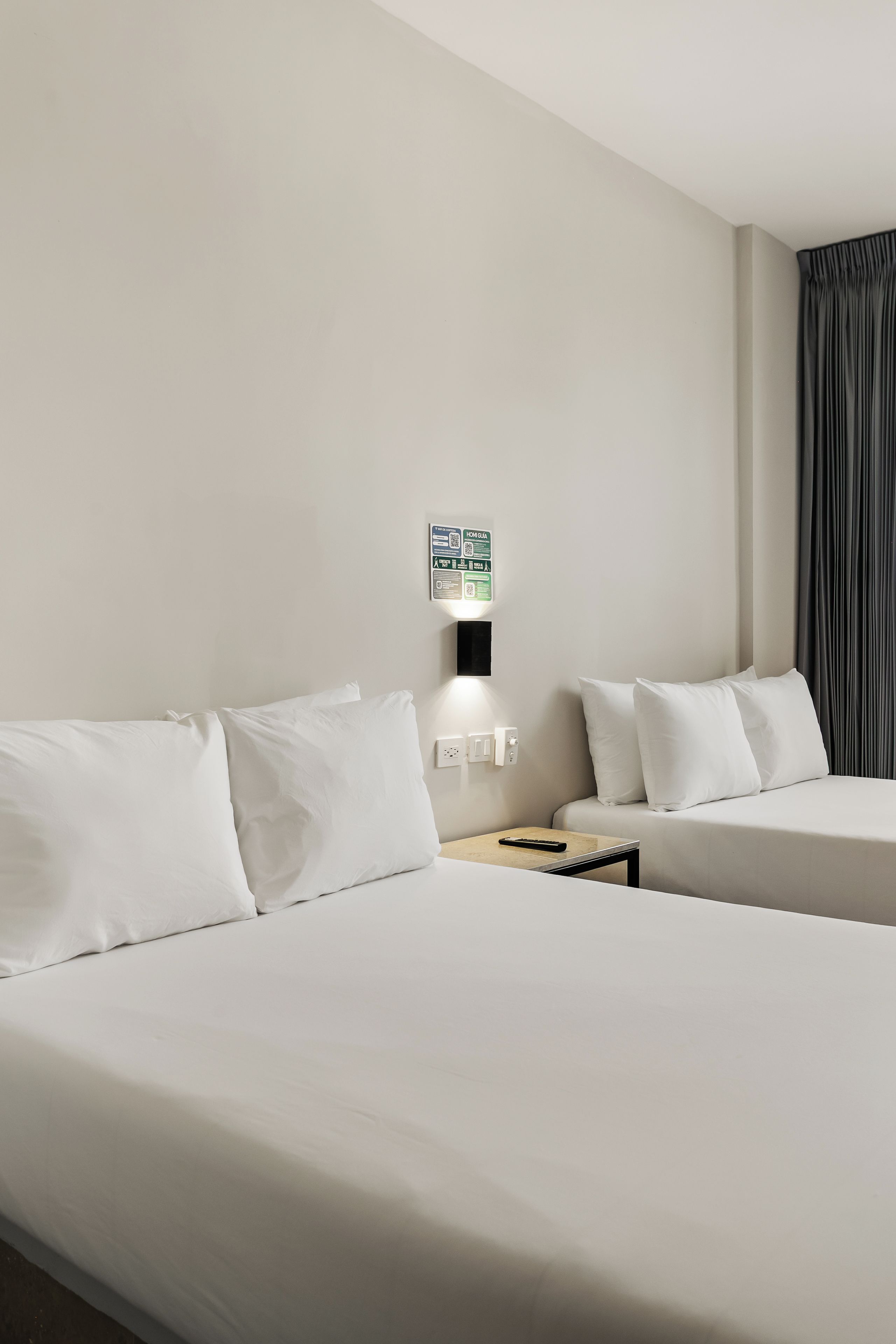 Habitación de hotel con dos camas, una mesita de noche, una lámpara y un letrero en la pared.