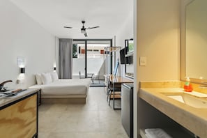 A hotel room with a bed, a desk, a chair, a dining table, a ceiling fan, and a bathroom with a sink and mirror. - Villa Maria Teresa By Homirent (Mérida)