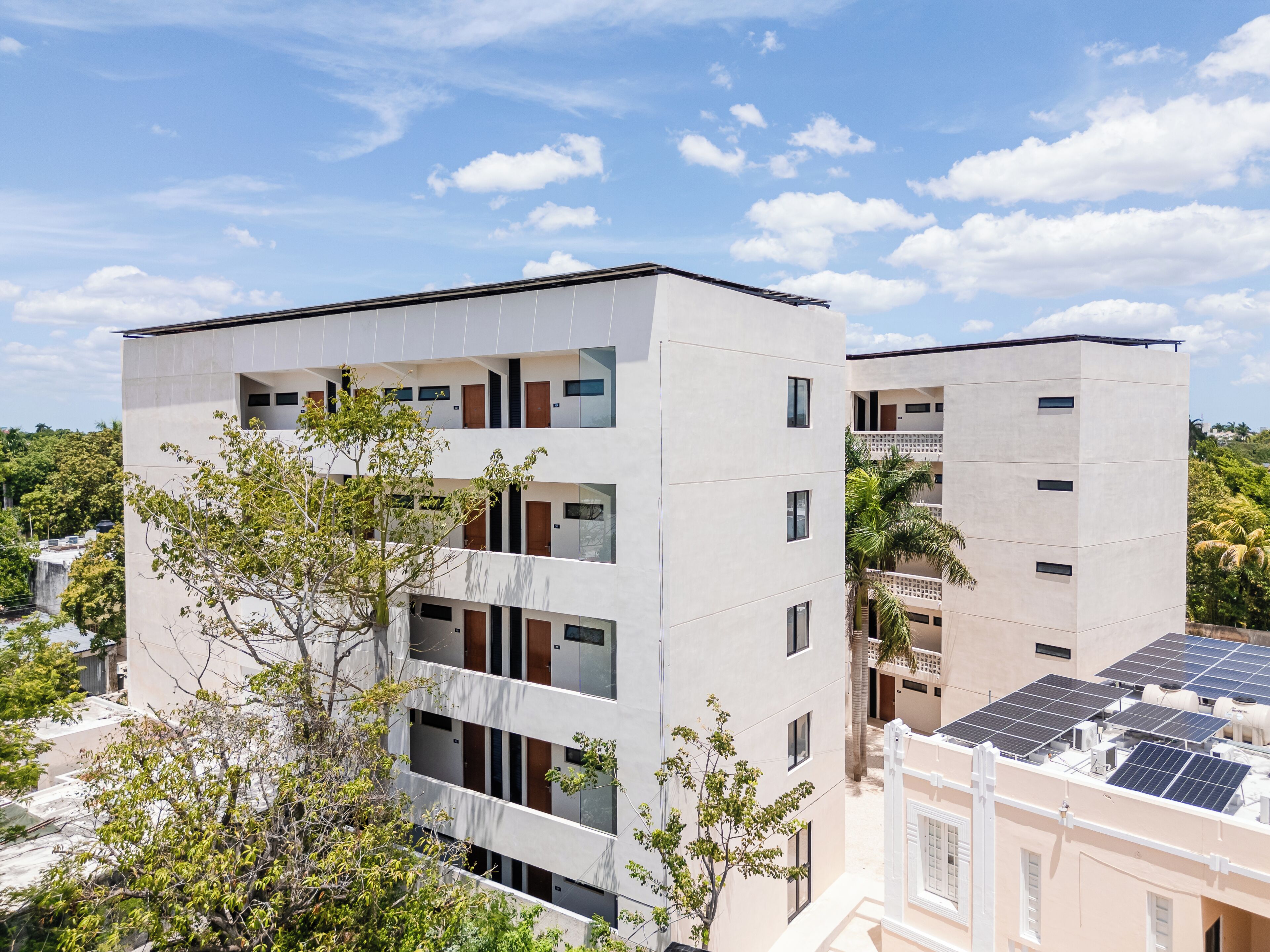 A modern multi-story building with balconies, large windows, and solar panels on the roof.