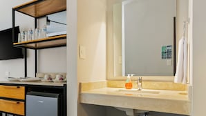 Un baño moderno con lavamanos, espejo, toallero y un refrigerador pequeño.