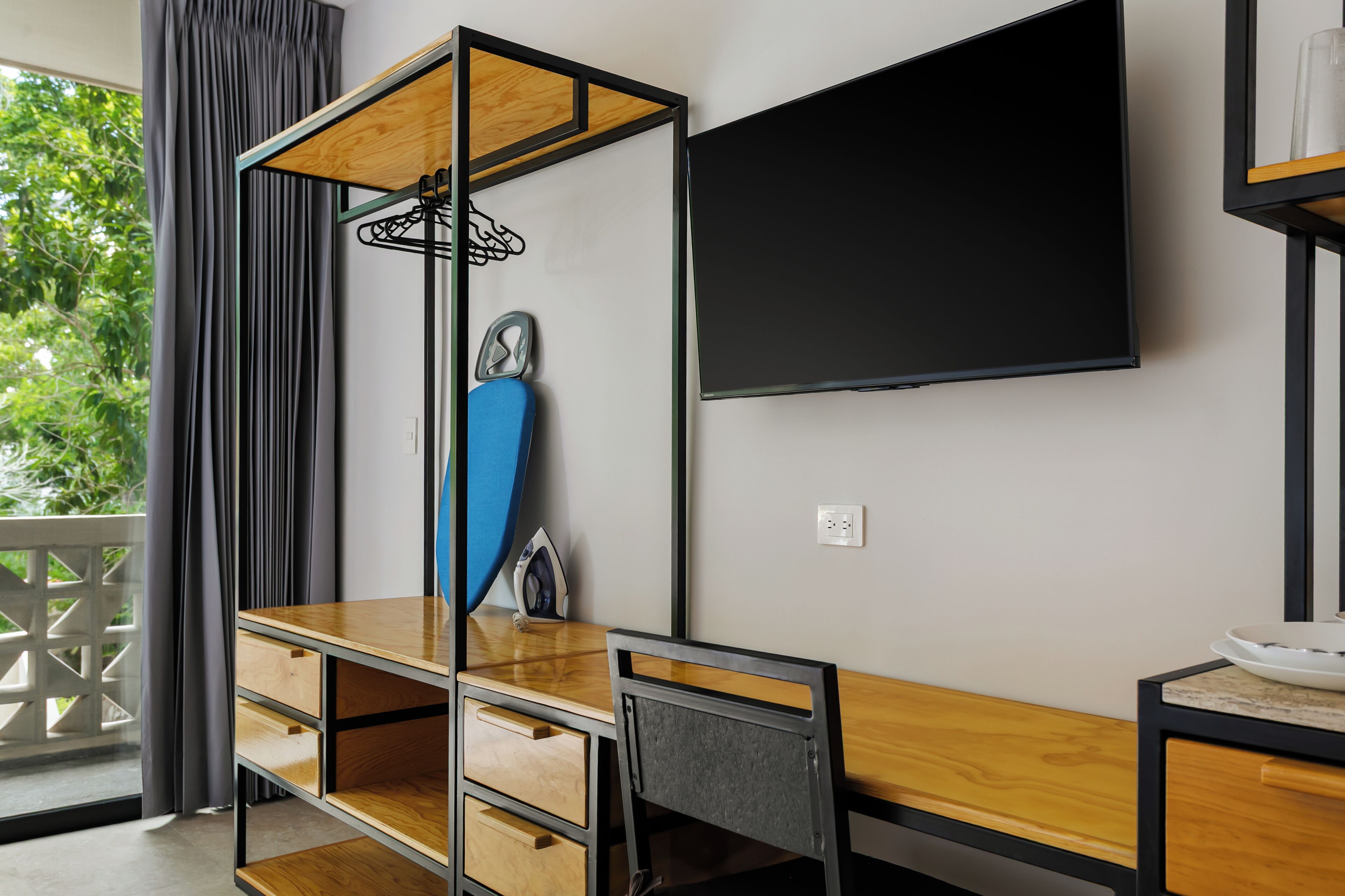 Quarto moderno com escrivaninha de madeira, uma cadeira azul, televisão e janela com cortinas.