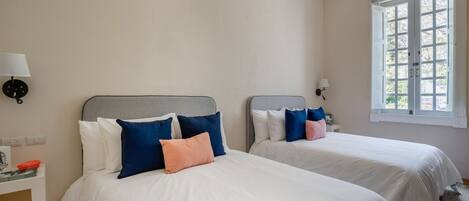 A hotel room with two beds, a window, and an air conditioning unit.
