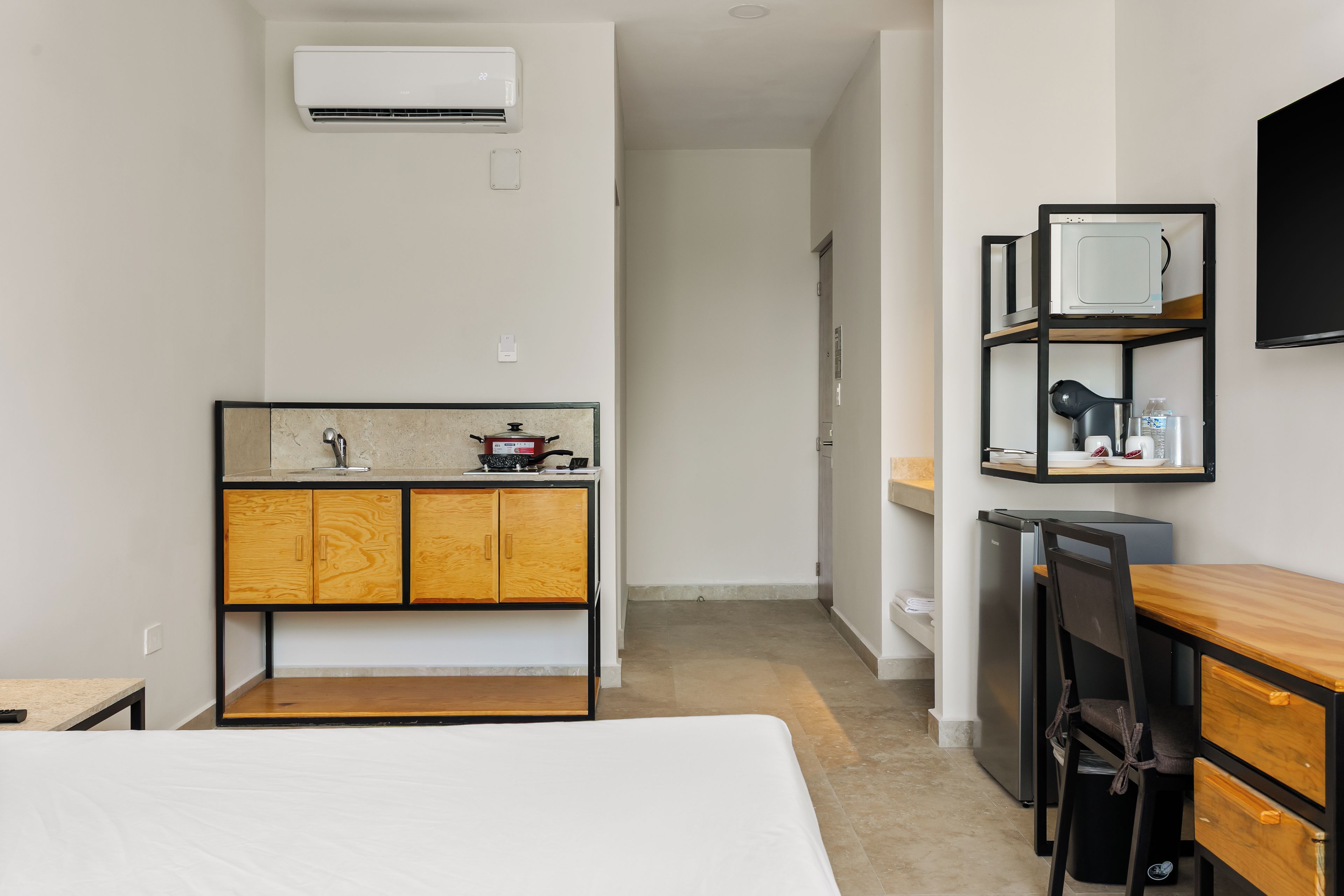 A compact hotel room with a bed, kitchenette, and a small seating area.