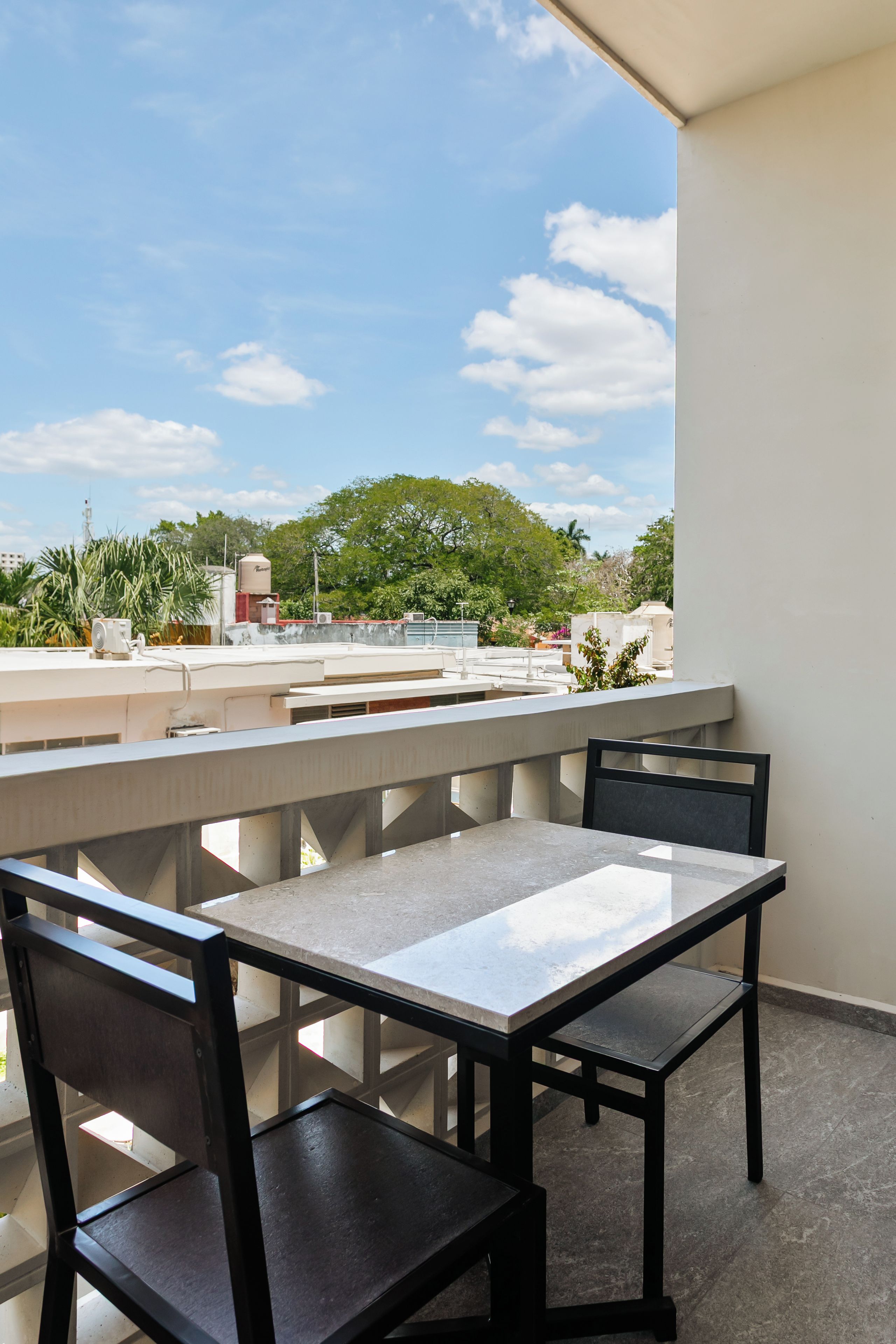 A balcony with a table and chairs, overlooking a cityscape with buildings and trees.