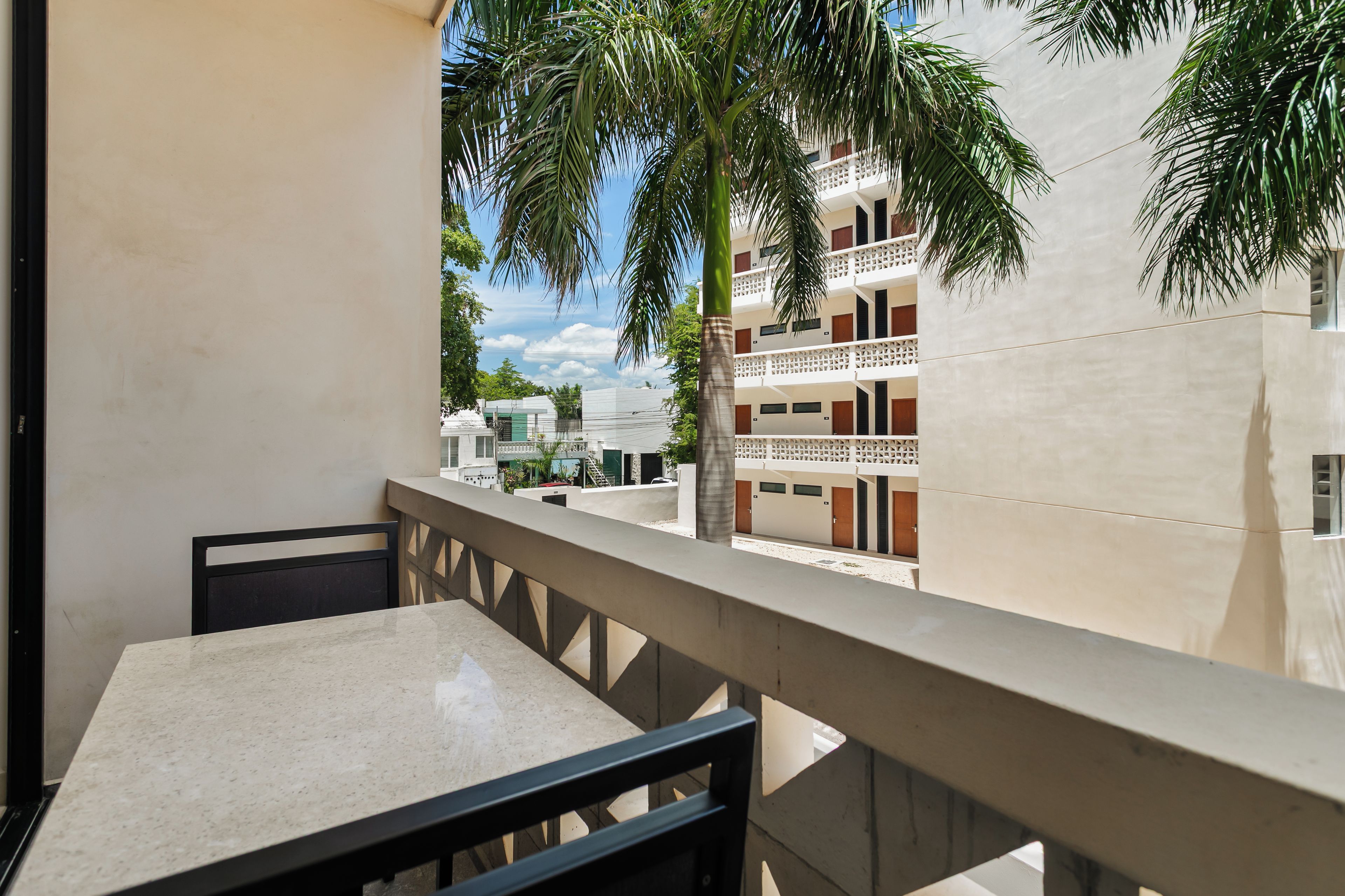 Un balcón con mesa y sillas, con vistas a un edificio con balcones y palmeras.