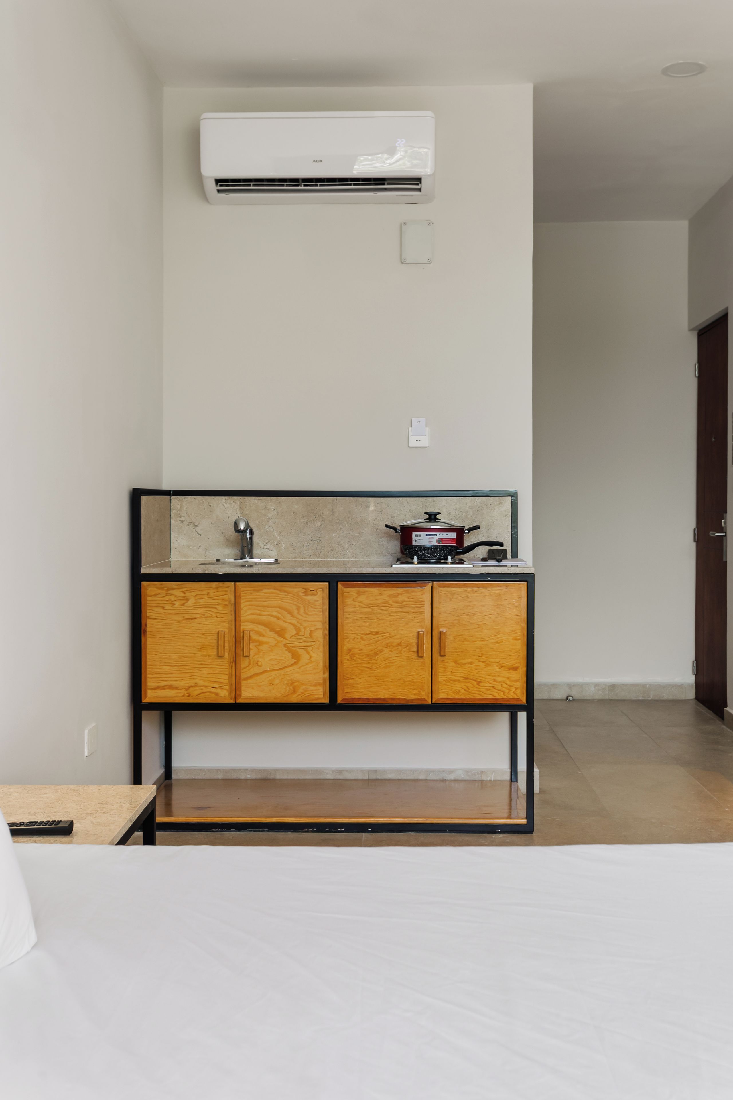 A hotel room with a wooden cabinet, a sink, and an air conditioner mounted on the wall.