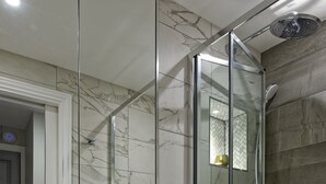 Een moderne badkamer met een douchecabine van glas, een wit toilet en een wand betegeld met marmer.