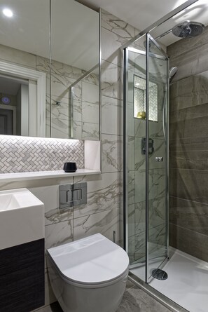 A modern bathroom with a glass shower enclosure, a white toilet, and a marble-tiled wall. - Standard studio by Dmontrio (London)