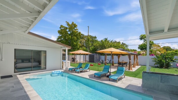 Una piscina con sillas de descanso, un porche cubierto y una casa con puerta corrediza de vidrio.
