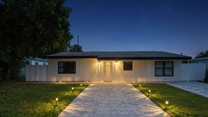 Una casa de dos pisos con un camino de entrada pavimentado, una puerta principal y un pequeño porche.