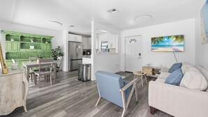 Una cocina moderna con armarios blancos, una pared de acento verde y una zona de comedor con mesa y sillas.