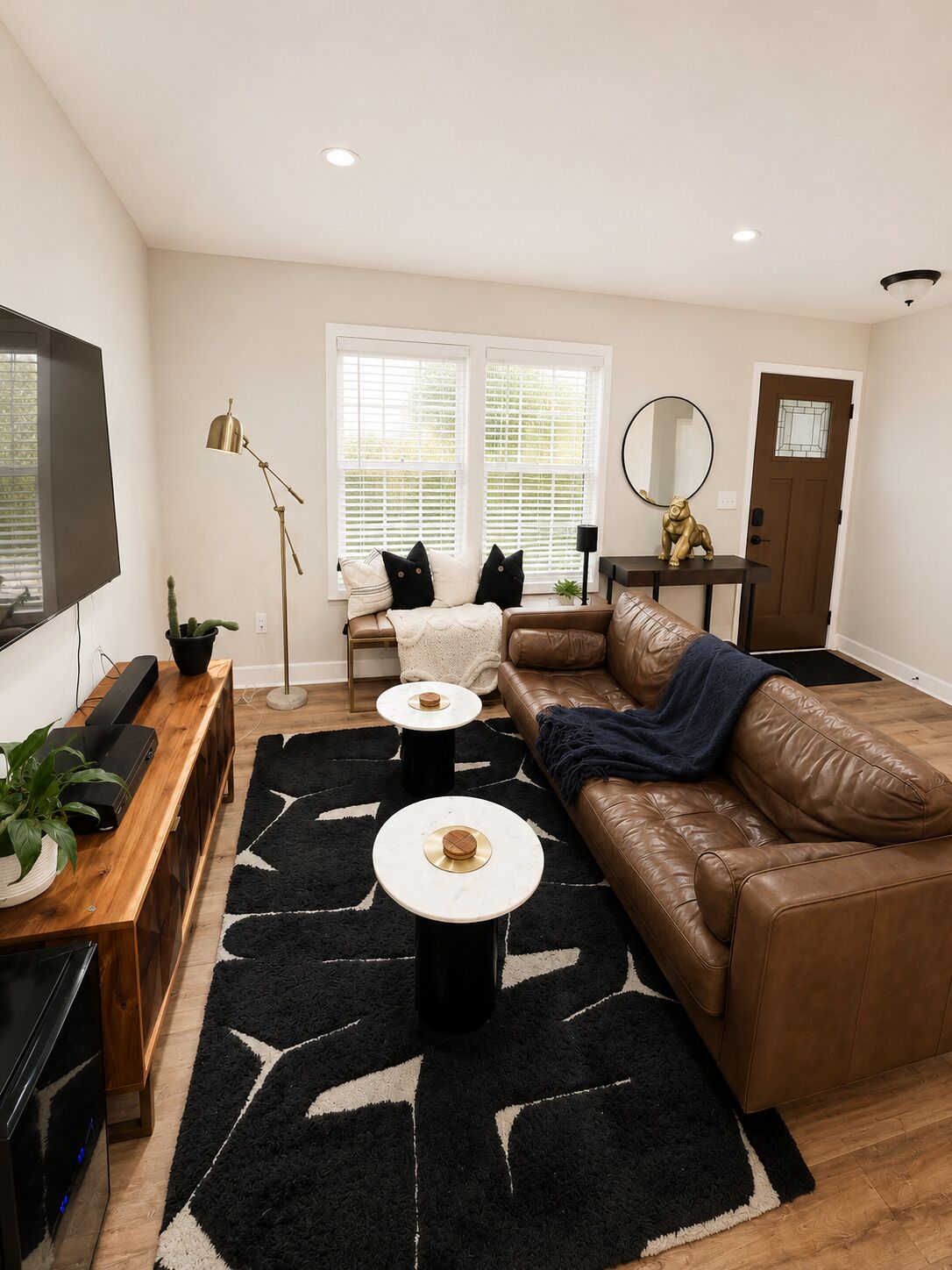 Een moderne woonkamer met een bruine leren bank, een televisie, een houten salontafel en een zwart tapijt.