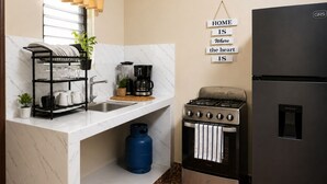 A compact kitchen with a gas stove, a refrigerator, a dish rack, and a sign that reads 'HOME IS where the heart IS.' - Casa Efra | Entire Home in Tela | A/C | 3BR | Sleeps 8 | Near Beach (Tela)