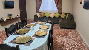 A dining area with a table set for four, a ceiling fan, a sofa, and a TV mounted on the wall. - Casa Efra | Entire Home in Tela | A/C | 3BR | Sleeps 8 | Near Beach (Tela)