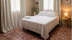 A hotel room with a bed, curtains, a nightstand with a lamp, a wall-mounted air conditioner, and a patterned floor. - Casa Efra | Entire Home in Tela | A/C | 3BR | Sleeps 8 | Near Beach (Tela)