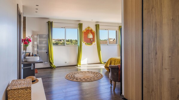 A spacious room with a large window, a wooden floor, a round woven rug, and a chair. - Casa Corsicana – appartement avec terrasse vue mer à Monticello (Monticello)