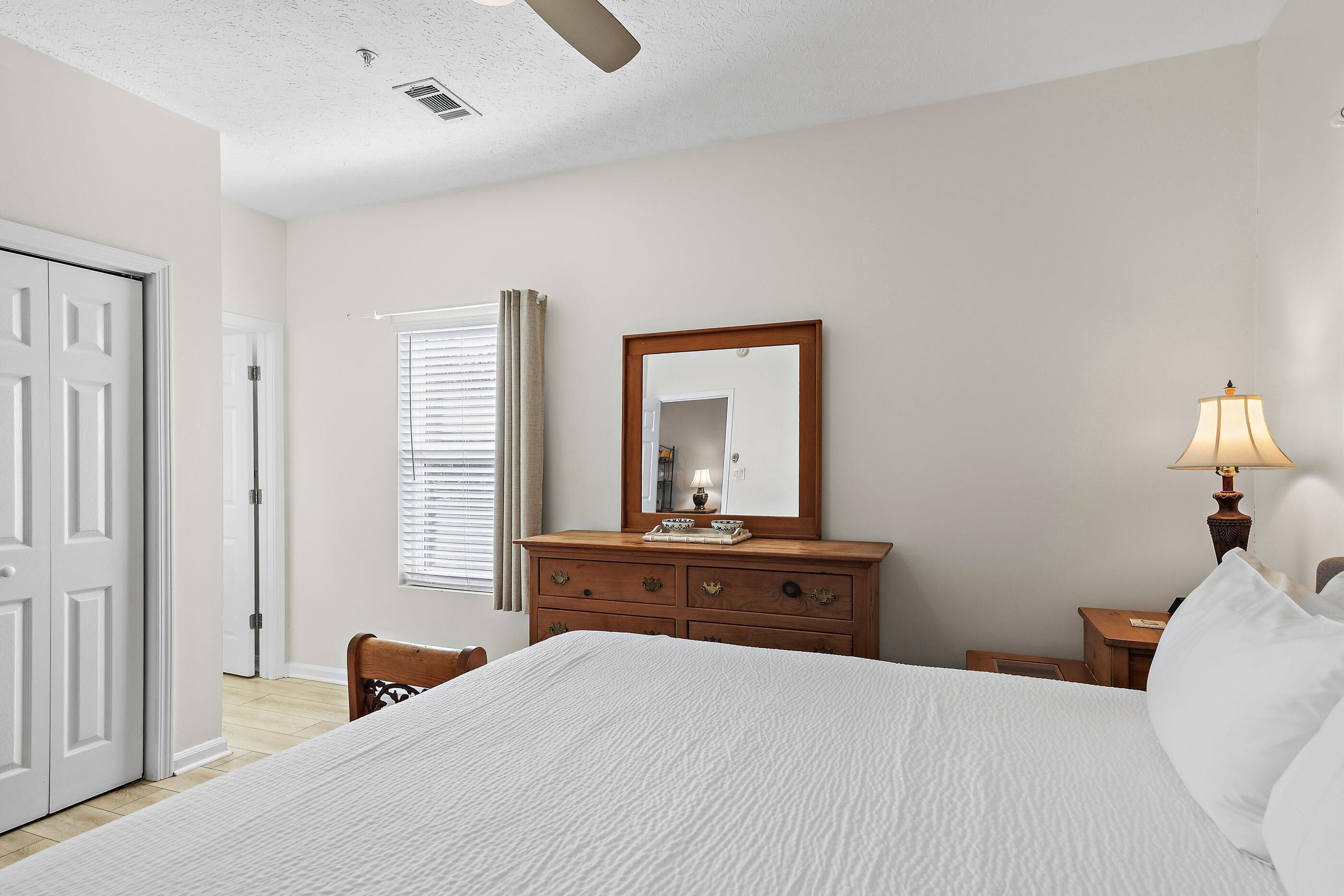 Une chambre à coucher avec un lit, une commode, un miroir, une lampe et une porte.