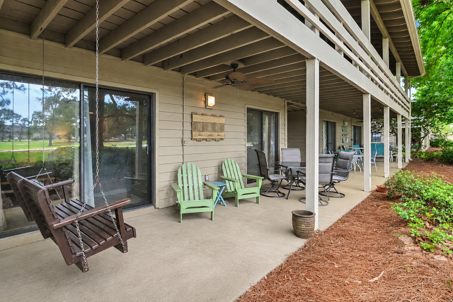 A covered porch with outdoor seating, including a swing, chairs, and a table.