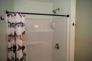 Une salle de bain avec un rideau de douche, une pomme de douche et une porte dotée d’une poignée.