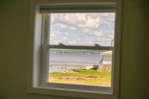 A window with a view of a body of water, a grassy area, and a building.