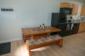 A kitchen with a wooden table and bench, a black refrigerator, and wooden cabinets.