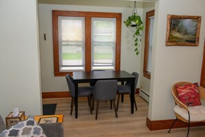 A dining area with a table and chairs, a hanging plant, and a painting on the wall.