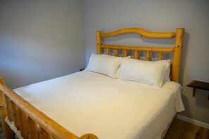 Ein hölzernes Bett mit Kopfteil, zwei Kissen und einer weißen Bettdecke in einem Zimmer mit schlichter Wand und einem kleinen Nachttisch.