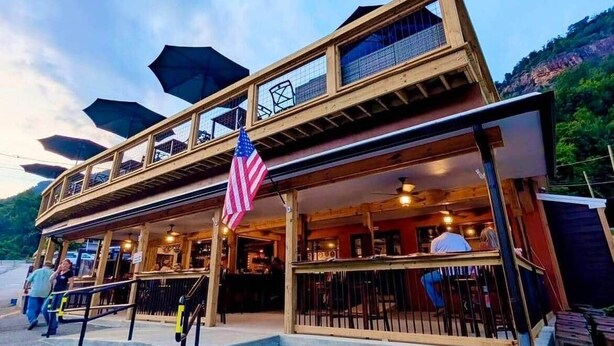 A two-story wooden building with a balcony, an American flag, and a view of the surrounding landscape. - Updated Chimney Rock cabin - Views & River Sounds (Chimney Rock)